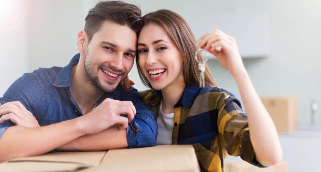 casal olhando para a câmera enquanto segura a chave do novo apartamento