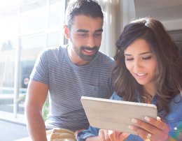 casal na sacada de casa lendo sobre as vantagens e desvantagens entre apartamento novo ou usado